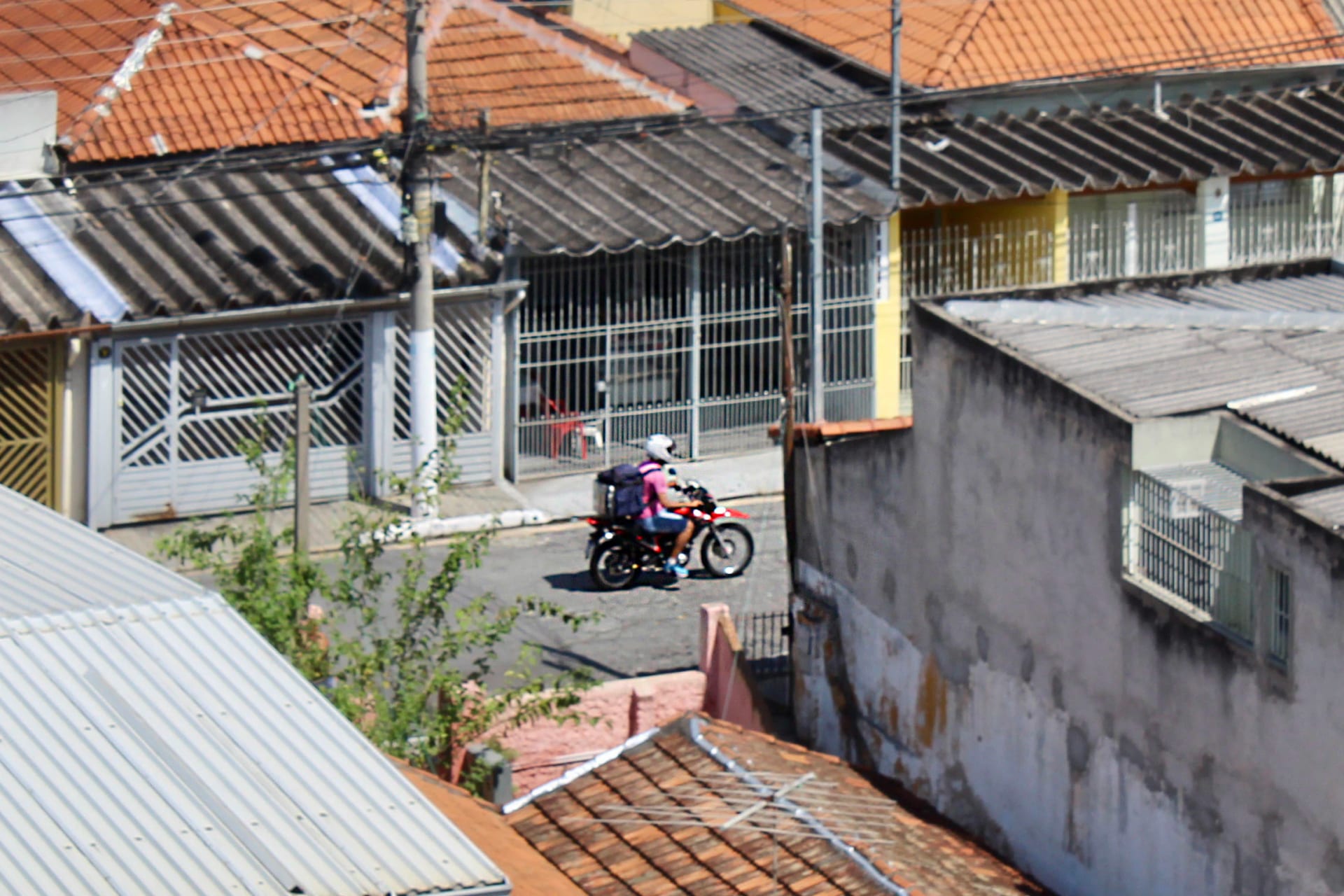 Entregador de aplicativo em alta velocidade sobre uma motocicleta, com a mochila térmica nas costas, numa rua brasileira